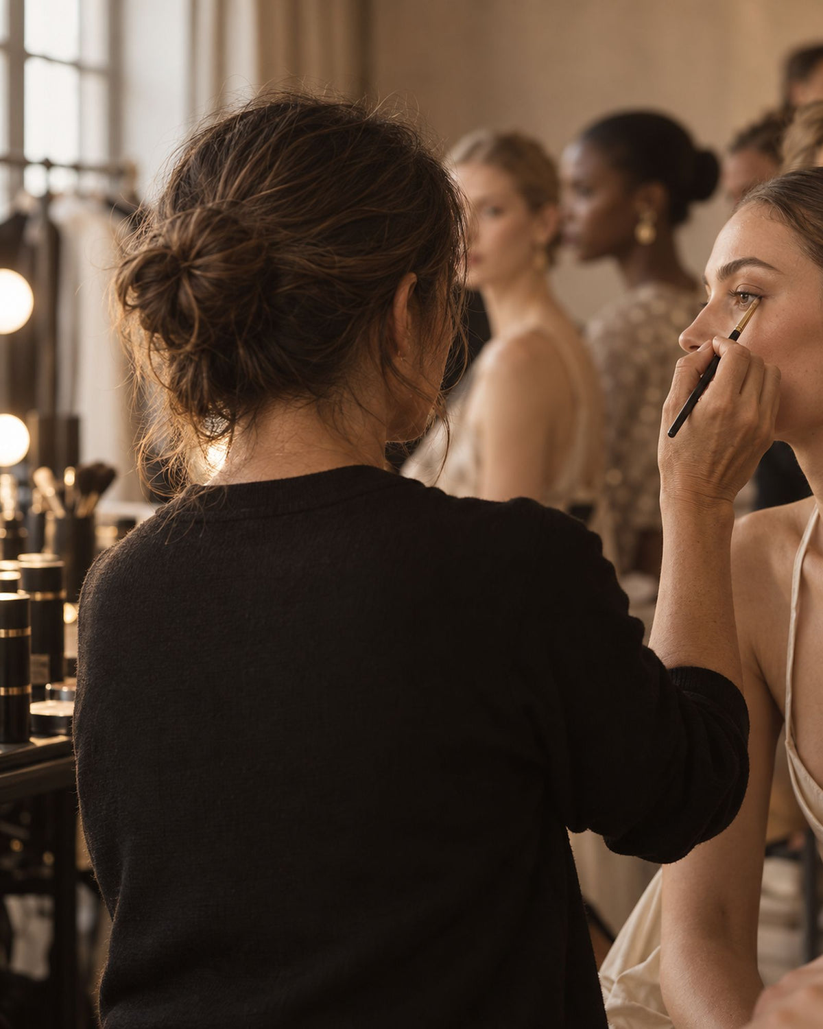 Maquilleuse vue de dos en coulisses de défilé, pinceau à la main